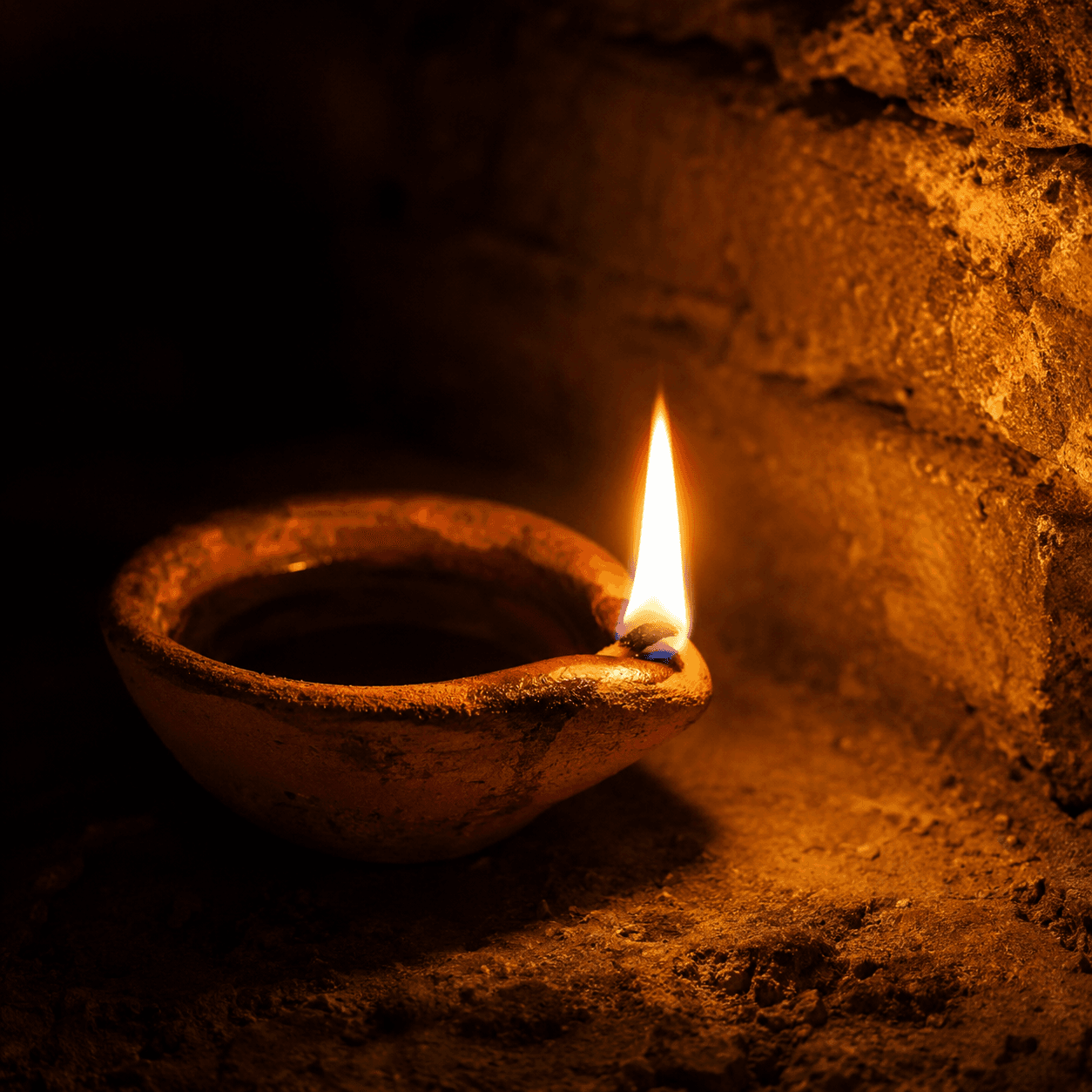 A small clay oil lamp burning with a single steady flame against a dark wall