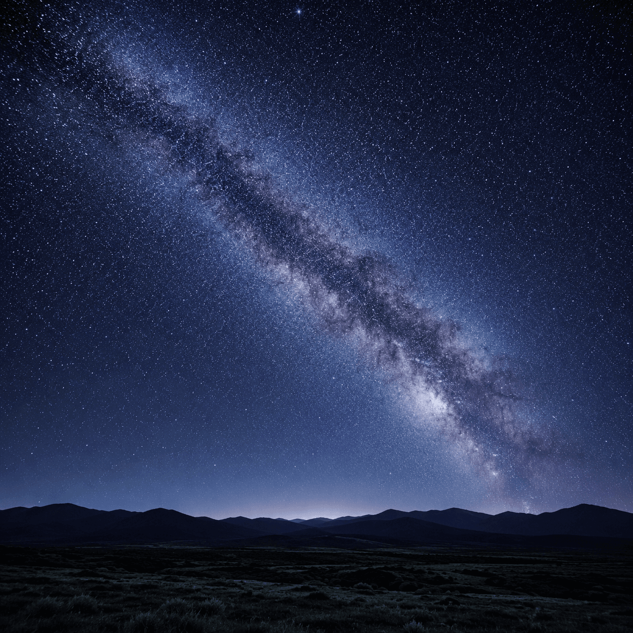 The Milky Way arching across a vast star-filled night sky over dark hills