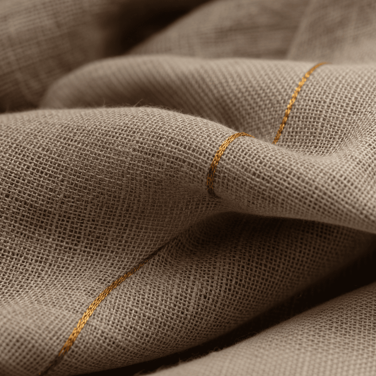 A single golden thread woven through natural linen cloth