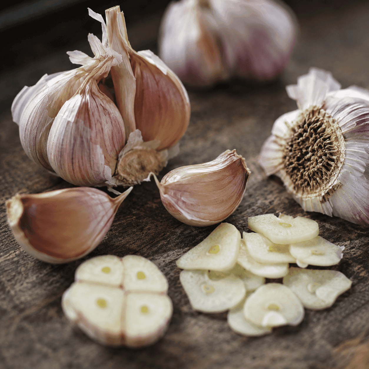 Split garlic bulbs and cloves with thinly sliced garlic on a dark rustic wood surface