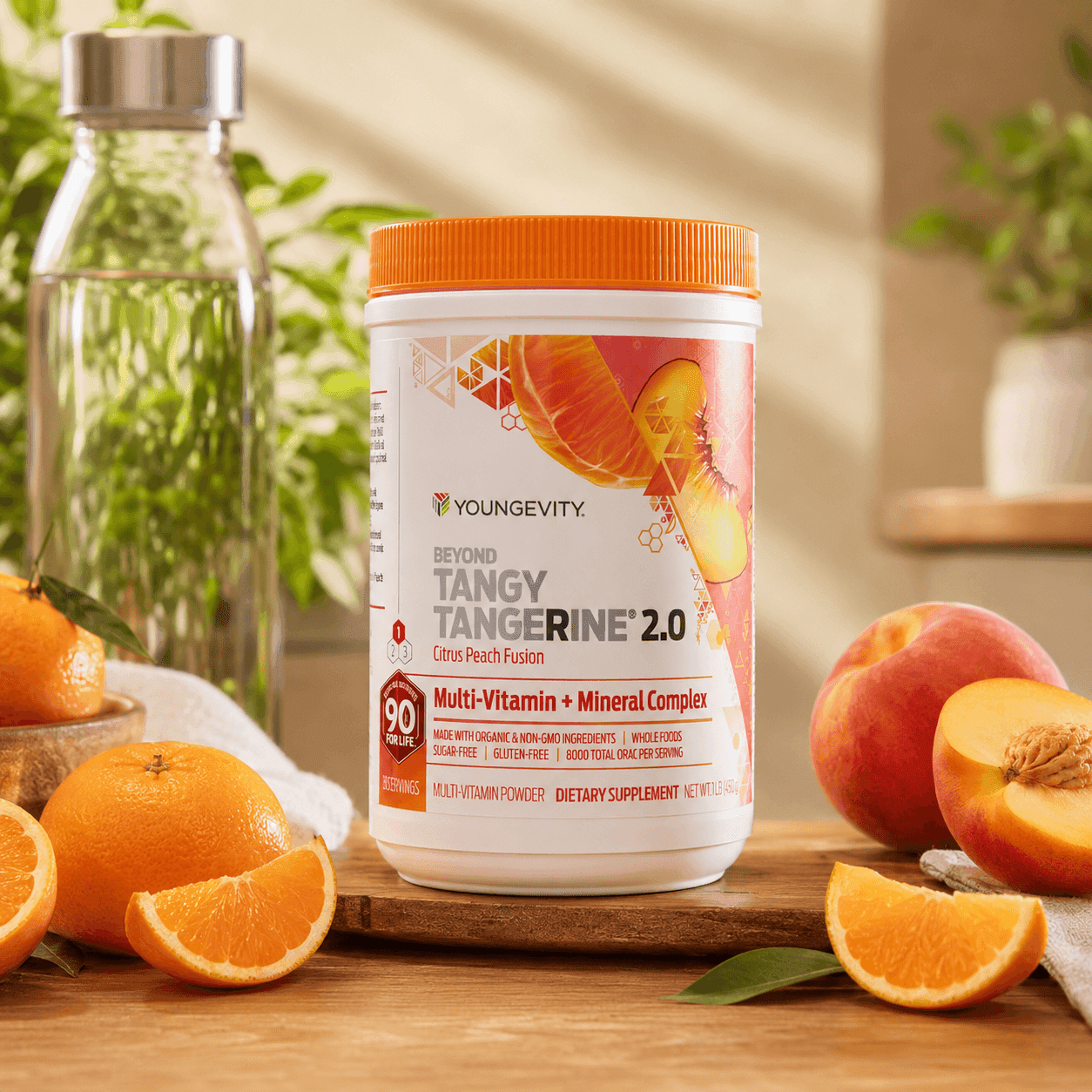 A container of Beyond Tangy Tangerine 2.0 on a wooden board surrounded by whole and sliced oranges, a peach, and a glass water bottle